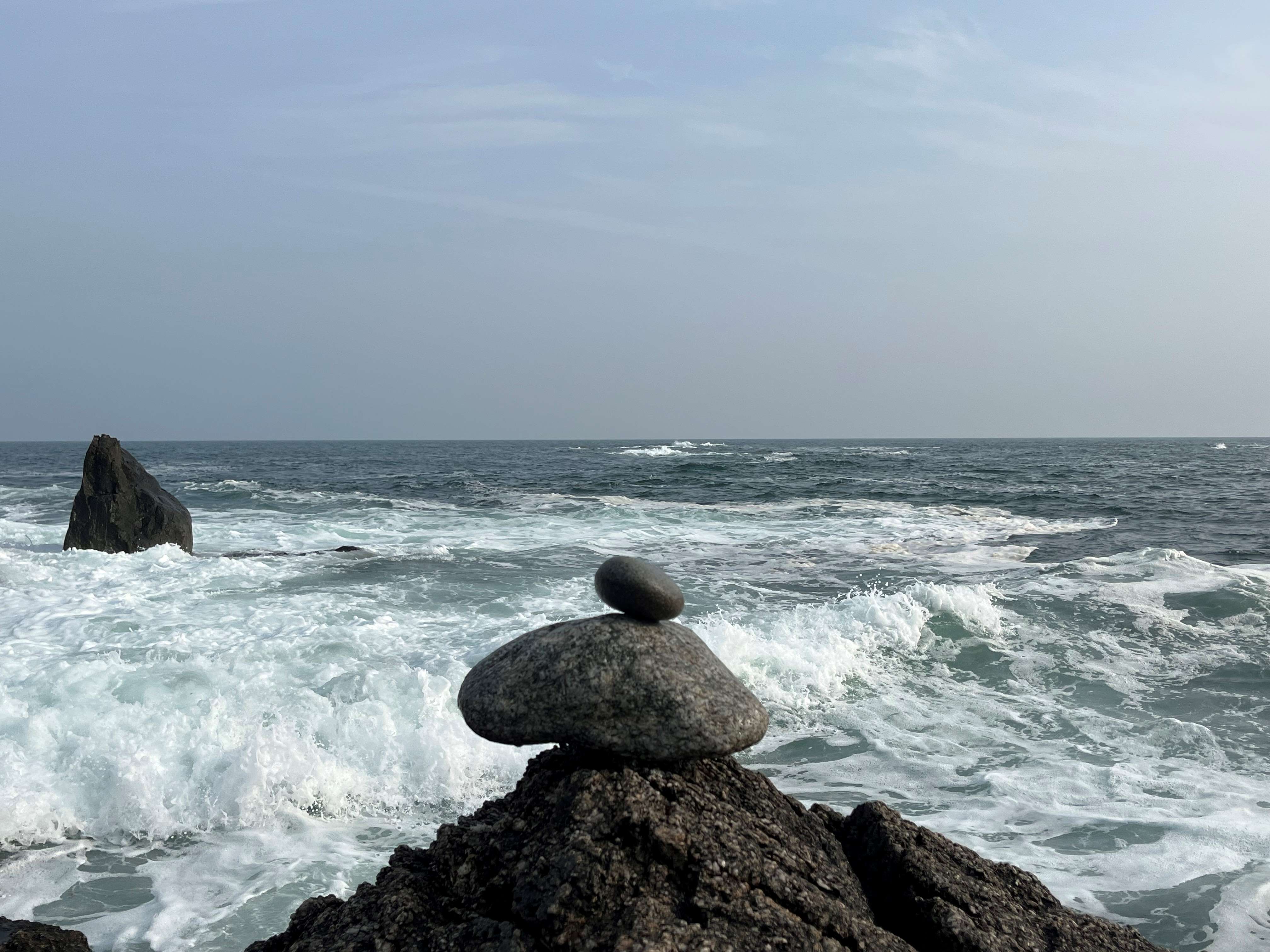 Two rocks balanced vertically, with the ocean in the background.