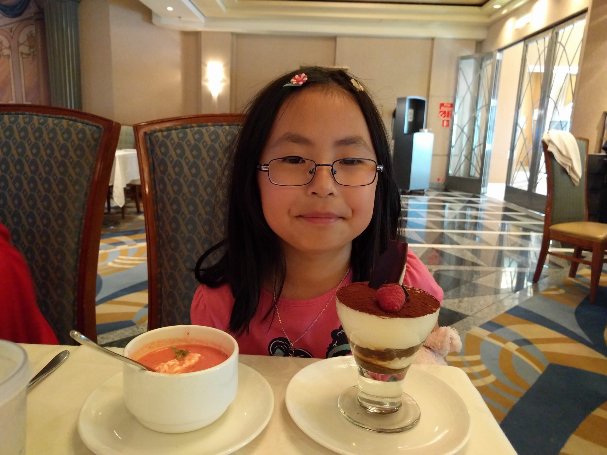 Young me smiling over a bowl of tomato soup and cup of tiramisu.