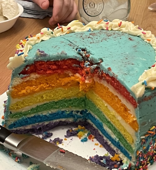 =Rainbow cake, sliced open with rainbow layers and blue frosting