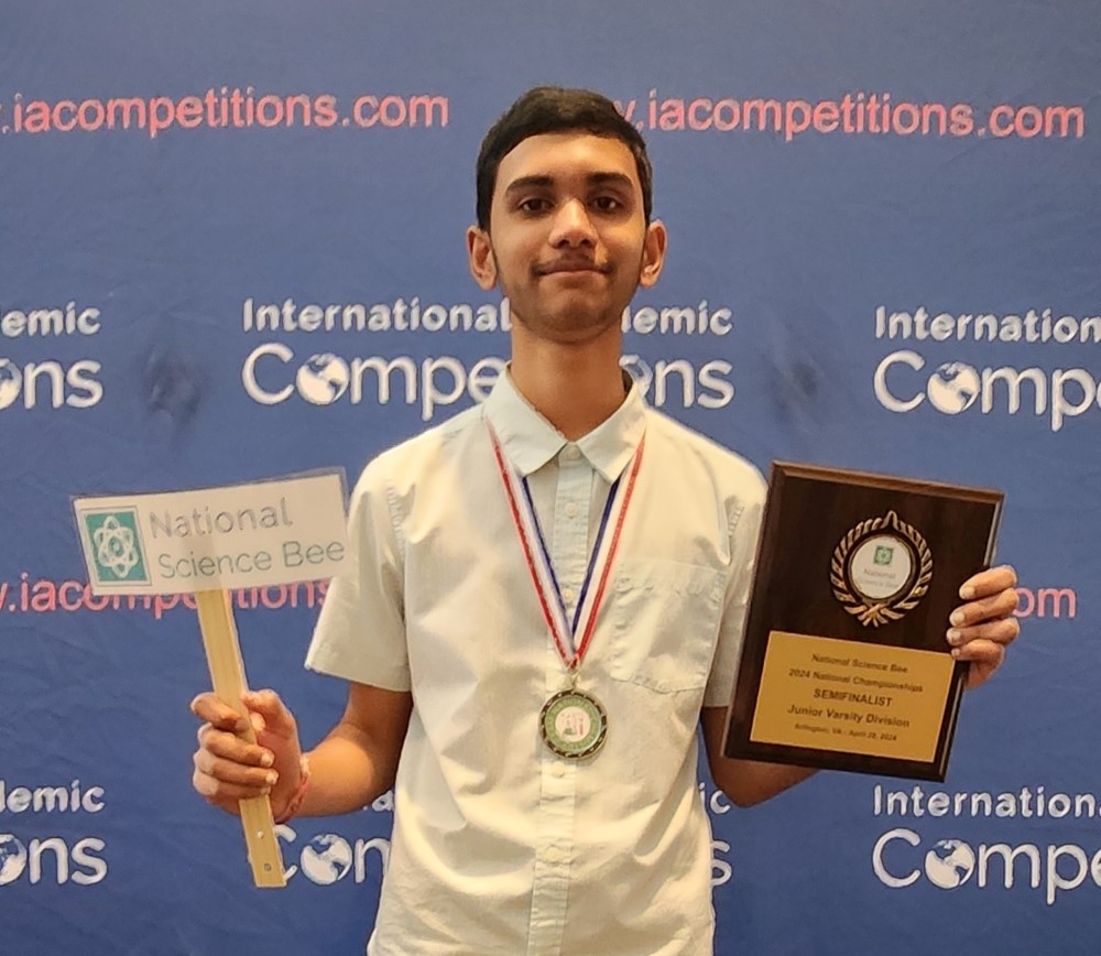 Photograph of Medhansh Choudhury posing with a National Science Bee
                Semifinalist plaque along with a National Chemistry Exam Runner-Up medal against an International Academic Competitions background.