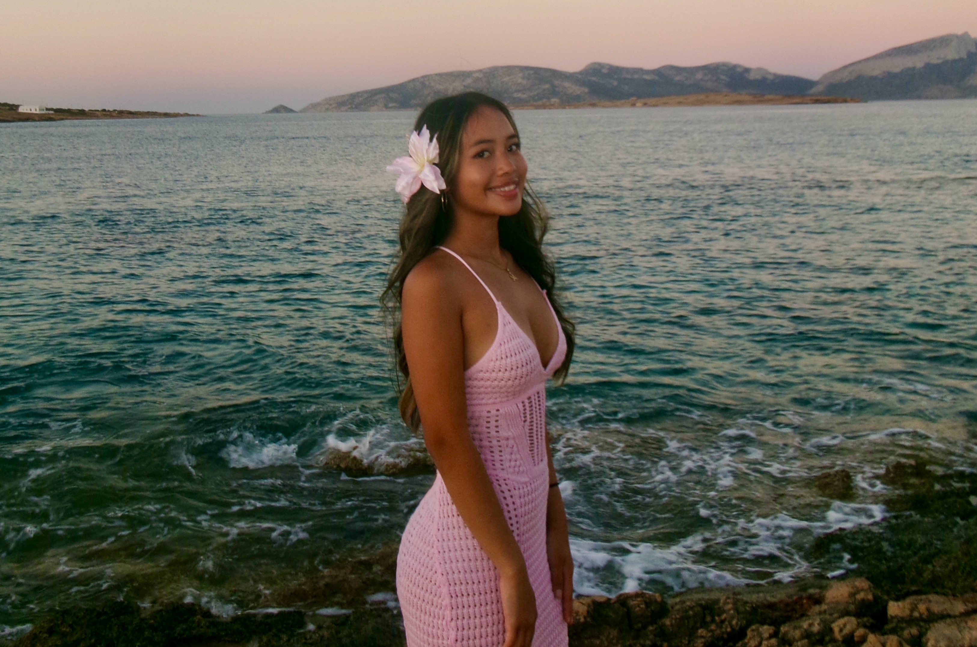 Girl in pink dress smiling in front of a beach