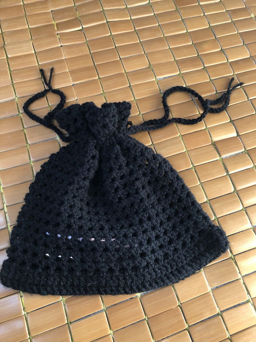 A black crocheted bag or pouch that closes 
					with a drawstring